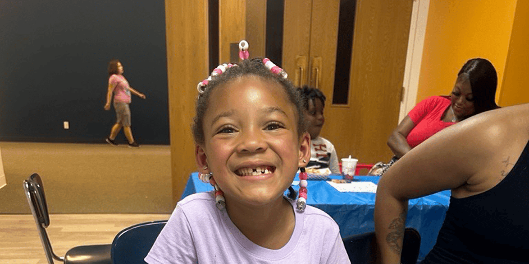 Smiling child with beaded braids looking at the camera.