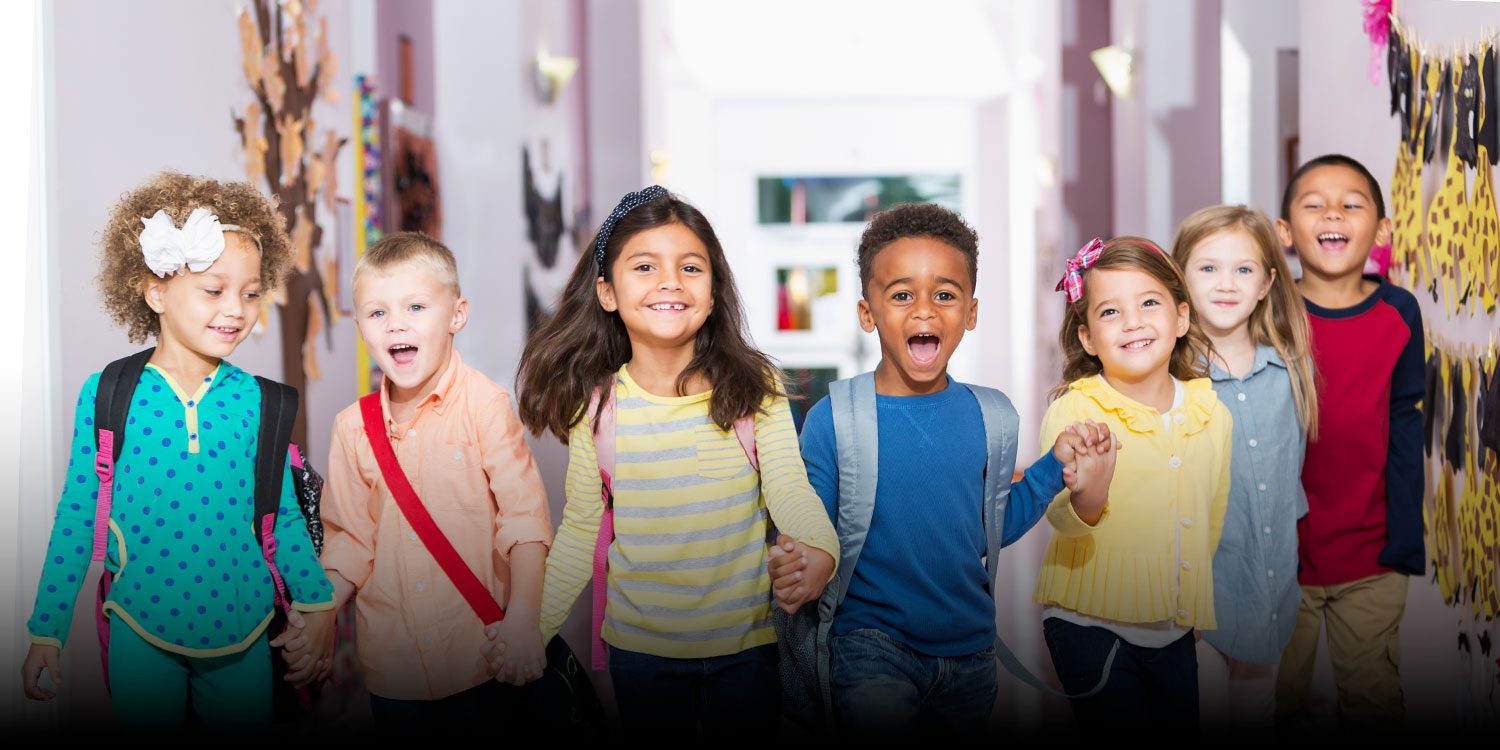 Smiling group of elementary students holding hands walking down a school hallway.
